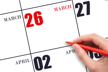 A hand holding a red pen and pointing on the calendar date March 26. Red calendar date, copy space,...
