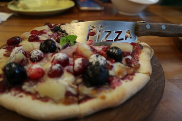 eating blue barry Pizza on the wooden plate close-up with pizzacutter