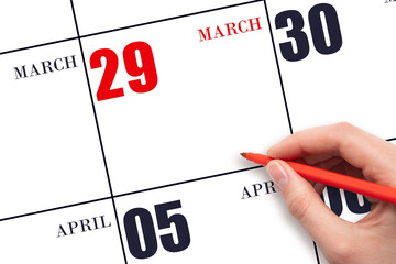 A hand holding a red pen and pointing on the calendar date March 29. Red calendar date, copy space,...