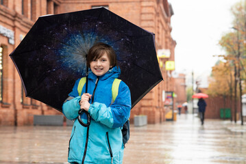 portrait of a smiling schoolboy with an umbrella on a rainy day outside