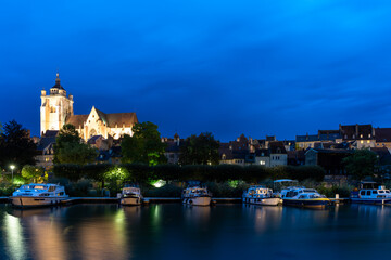 Fototapeta na wymiar nightime view of the illuminated Notre Dame catholic church in Dole with houseboats on the Doubs River in the foreground