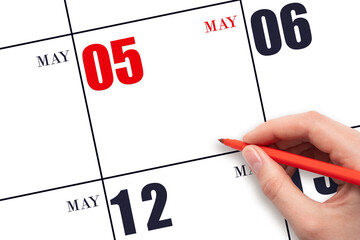 A hand holding a red pen and pointing on the calendar date May 5. Red calendar date, copy space,...