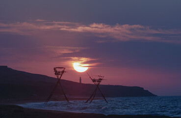 majestic sunrise over the sea against the backdrop of a lighthouse and fishing structures