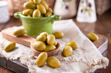 Large green olives in a cup on a wooden table. Italian olives, Sardenya and Greece harvest. Olive oil is poured on the berries, olive leaves in the frame. close-up. Copy sapce