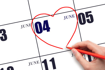 A woman's hand drawing a red heart shape on the calendar date of 4 June. Heart as a symbol of love.