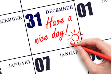 The hand writing the text Have a nice day and drawing the sun on the calendar date December 31