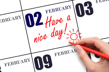 The hand writing the text Have a nice day and drawing the sun on the calendar date February 2