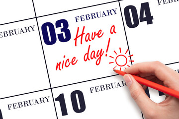 The hand writing the text Have a nice day and drawing the sun on the calendar date February 3