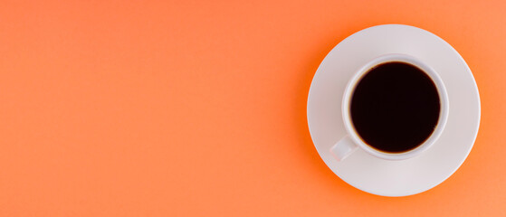 White cup with coffee on saucer on orange coral background. Black coffee for breakfast. Top view. Panoramic shot