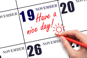 The hand writing the text Have a nice day and drawing the sun on the calendar date November 19