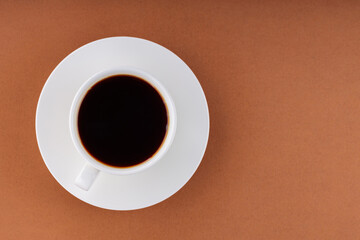 Obraz na płótnie Canvas Coffee cup on a brown background. Cup of black coffee on a white saucer. Top view. Copy space