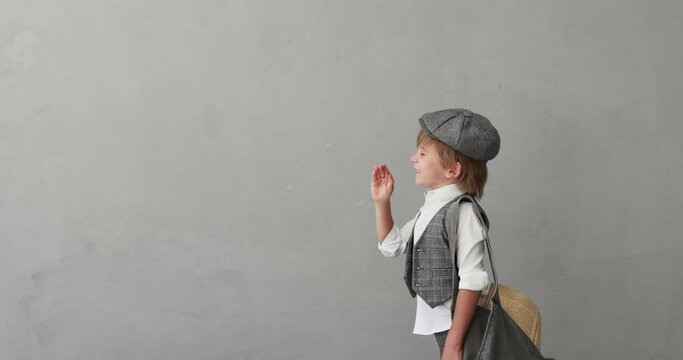 Newsboy shouting against concrete wall background. Child wearing vintage costume. Kid holding newspaper. Slow motion