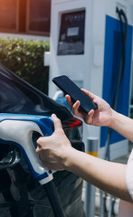 Hand plugging in a charger in an electric car socket.Electric car or ev is charging at station