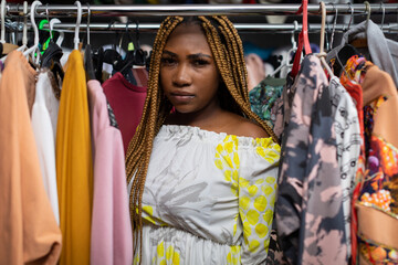 The serious face of the dark-skinned girl standing among the hanging clothes.
