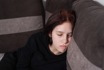 Young teenage girl tired after studying at school and fell asleep on sofa at home after reading school literature, beautiful teenage girl napping