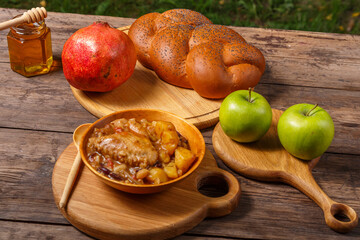 Chelnt with chicken in a wooden plate on the festive table for Rosh Hashanah next to challah honey...