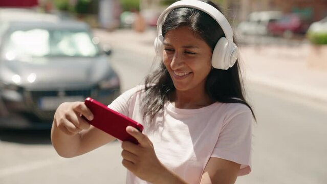 Young beautiful hispanic woman smiling confident playing video game at street