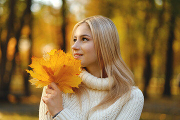 Young beautiful blonde woman in a white sweater walks in the autumn park.