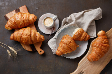 Kitchen boards, gray napkin, plate and cup of coffee with tasty croissants on rusty table. Fresh...