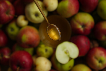 Close-up of a golden spoon with honey on a background of ripe colored apples