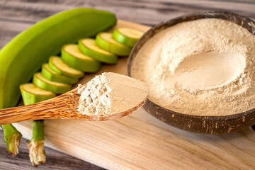 Spoonful of organic green banana flour on a backdrop of tasty bananas. © Anastasiia