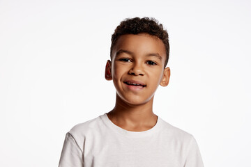 Fototapeta Smirk. Half-length portrait of african little boy in white tee expressing emotions isolated over white background. Kids emotions concept obraz