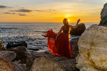 a dancing woman in a red flying dress on the ocean or on the sea beach against the backdrop of the sunset sky.