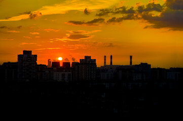 Bright colorful sunset, cloudy sky. Twilight, cityscape. Silhouettes of buildings, pipes and cooling towers of a thermal power plant against a bright sky. Moscow, evening landscape. Background