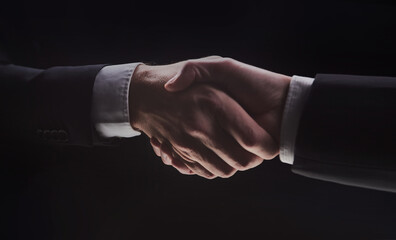 Photo of two men in suits shaking hands on a black background