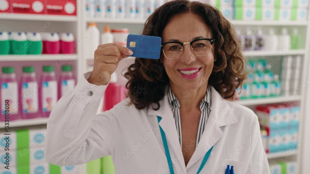 Sticker middle age woman pharmacist smiling confident holding credit card at pharmacy