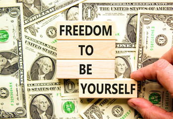 Freedom to be yourself symbol. Concept words Freedom to be yourself on wooden blocks on beautiful background from dollar bills. Businessman hand. Business, psychological freedom to be yourself concept