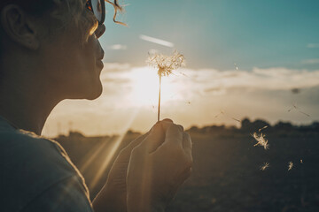 Day dreaming leisure activity with woman blowing a dandelion outdoor in the nature park. Emotion...