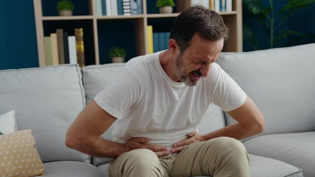 Middle age man suffering for stomach ache sitting on sofa at home