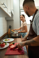 Man cuts vegetables and communicates with his wife in kitchen