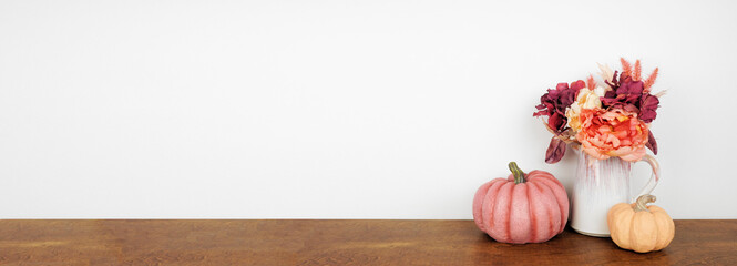 Autumn decor on a wood shelf against a white wall banner background. Pumpkins and flowers of pink...