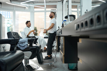 Friendly barber and his guest laughing together before hair-grooming