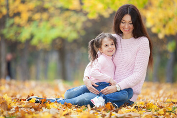 Happy mother and daughter in the autumn park. Beauty nature scene with family outdoor lifestyle. Happy family resting together on green grass, having fun outdoor. Happiness and harmony in family life - 533016025