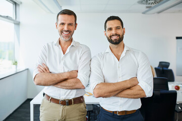 Two business partners standing together in modern office. Portrait of two businessmen in office looking at camera