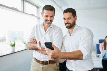 Two businessmen standing in office discussing looking on the phone