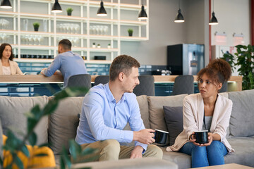 Woman and her colleague sitting on sofa at coffee break