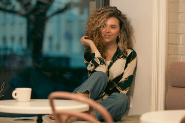 Fototapeta na wymiar Pretty Young Woman With Curly Hair Relaxing In Cafe
