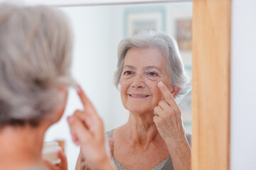 Portrait of senior beautiful woman applies anti aging cream on wrinkled face - elderly smiling lady...