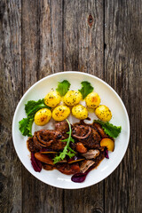 Roast pork loin with plums and fried potatoes on wooden table
