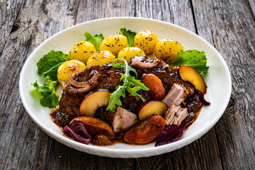 Roast pork loin with plums and fried potatoes on wooden table
