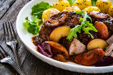 Roast pork loin with plums and fried potatoes on wooden table
