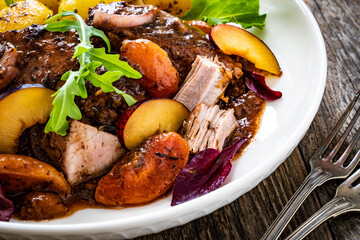 Roast pork loin with plums and fried potatoes on wooden table
