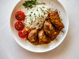 Wrapped pork served with white rice and cherry tomatoes  on white table