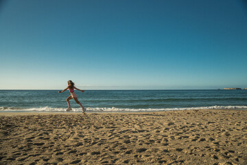 Side view of girl running on the beach towards the blue sea on beautiful sunny day