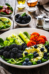 Fresh salad - avocado, blackberries, cucumber, cherry tomatoes, blueberries and greens on wooden table
