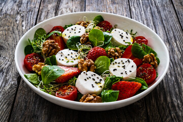 Fresh salad - goat cheese, strawberries, walnuts, cherry tomatoes and leafy greens on wooden table
